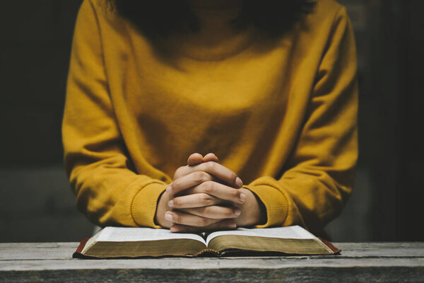 Woman praying on holy bible in the morning. Holding hands in prayer on a wooden table. Christian life crisis prayer to god. Hands folded in prayer on a Holy Bible in church concept for faith.
