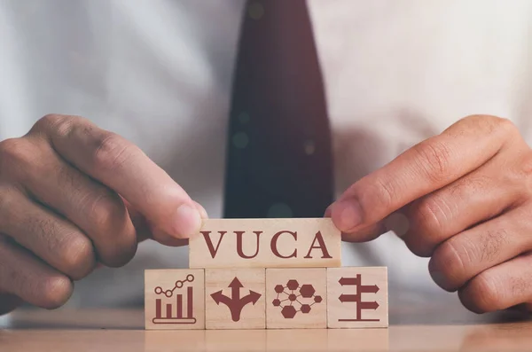 VUCA ve stratejik yönetim. El, VUCA simgesi ve metin uçuculuğu olan tahta küpleri, belirsizlik, karmaşıklık, gri arkaplan ile belirsizlik koyar. Yeni eğilim ve hızlı geçiş için akıllı yönetim. 