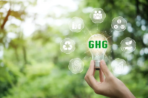 Hand holding light bulb with GHG greenhouse gas on a beautiful green background. Business and GHG concept. Copy space. Greenhouse gas symbol.