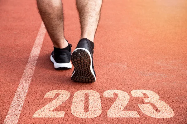 Goals and plans for the next year. Rear view of a man preparing to start on an athletics track engraved with the year 2023