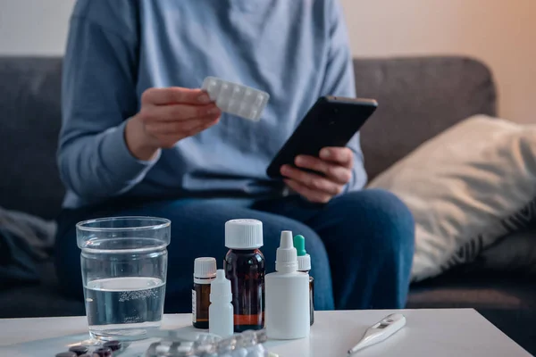 Medicine on the bedside table and woman checking information about pills in the Internet on the background.