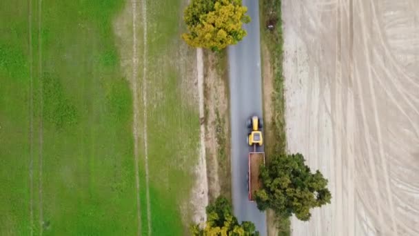 Traktor vezetés burgonyával egy kis úton Lengyelországban. Drónlövés. Légi felvétel, felülnézetből. Mozgókép. — Stock videók