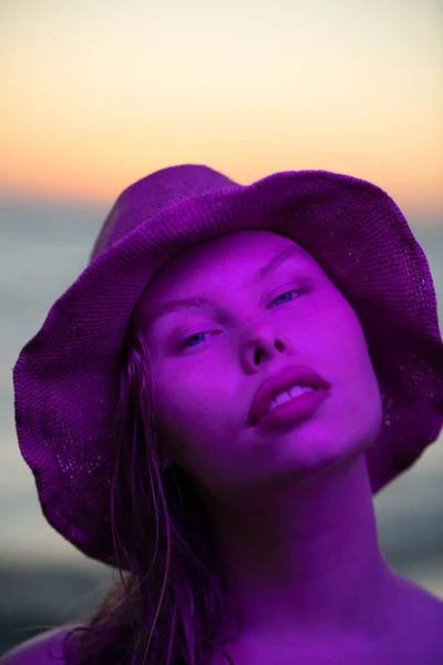 Modèle courbé tendance avec un visage confiant dans la lumière du néon violet avec un coucher de soleil en arrière-plan. — Photo
