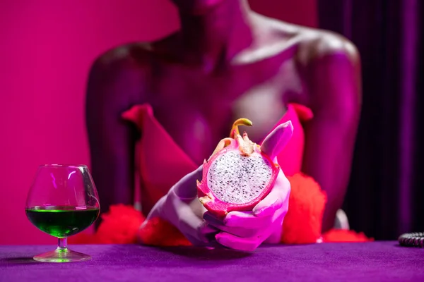 Black model holding sliced dragon fruit in exotic pink purple setting with a green cocktail. . High quality photo