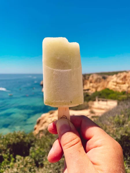 Hand Holding Ice Cream Blue Sea Cliffs Algarve Portugal Background — Stockfoto