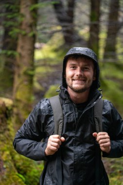 Kameraya gülümseyen mutlu yürüyüşçü. Ormanda yağmur. Sırt çantası. Yüksek kalite fotoğraf