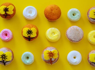 Pudra şekeriyle süslenmiş sıra sıra muffinler ve sarı arkaplanda krema şeklinde sarı çiçekler.