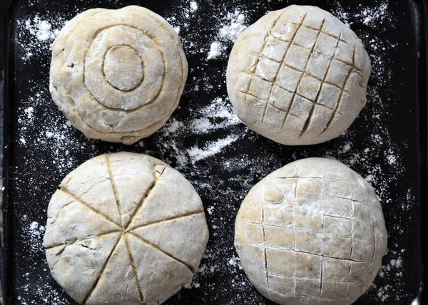 Round and raw loaves of bread on a black background floured and cut in for decoration