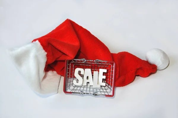 Beyaz arkaplanda, Noel Baba şapkasında alışveriş torbası satışı yazıyor. Noel indirimi kavramı, beyaz arka planda Xmas pazarı hediyesi. Seçici odak