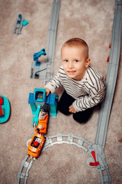 Evde oyuncak tren yolunda plastik trenle oynayan mutlu bir çocuk..