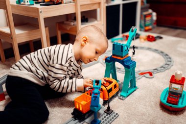 Evde oyuncak tren yolunda plastik trenle oynayan mutlu bir çocuk..