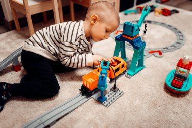 Evde oyuncak tren yolunda plastik trenle oynayan mutlu bir çocuk..