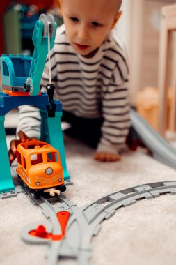 Evde oyuncak tren yolunda plastik trenle oynayan mutlu bir çocuk..
