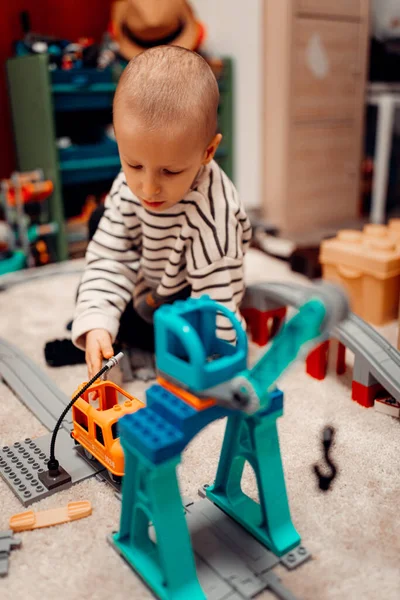 Evde oyuncak tren yolunda plastik trenle oynayan mutlu bir çocuk..