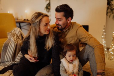 Genç çift, küçük kızlarıyla birlikte Noel için dekore edilmiş evde eğleniyorlar.