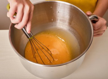 Kız mutfakta ev yapımı bir pasta hazırlıyor. Eller çırpılmış yumurtaları metal bir kasede çırpar. Yakın plan. Yüksek kalite fotoğrafçılık