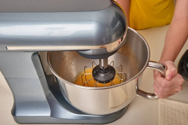 Uma menina cozinha bolo caseiro na cozinha, bate ovos em uma misturadora na mesa da cozinha. Close-up. — Fotografia de Stock