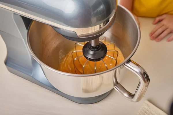 A girl cooks homemade cake in the kitchen, beats eggs in a mixer on the kitchen table. Close-up.