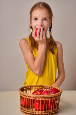 Mutlu bir çocuk, elinde taze kırmızı elmalar tutan gülümseyen bir kız. Yakınlarda elmalı bir sepet var. Gri arka planda güzel bir kızın portresi. Sağlıklı ve organik kavramı