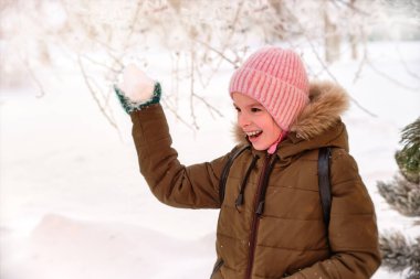 Mutlu, gülümseyen komik bir çocuk, kışın dışarıda yürüyen, karla oynayan bir kız. Güneşli bir kış günü.