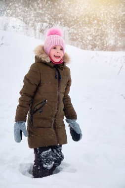 Mutlu, gülümseyen komik bir çocuk, kışın dışarıda yürüyen, karla oynayan bir kız. Güneşli bir kış günü.