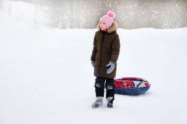 Kar borusunda karlı bir tepeden kayan, karlı havada parkta kızak kayan aktif mutlu bir kız. Kış mevsiminde sağlıklı yaşam biçimi kavramı.