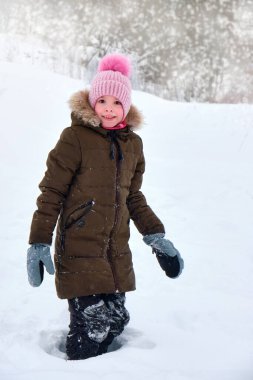 Mutlu, gülümseyen komik bir çocuk, kışın dışarıda yürüyen, karla oynayan bir kız. Güneşli bir kış günü.