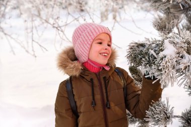 Mutlu, gülümseyen komik bir çocuk, kışın dışarıda yürüyen, karla oynayan bir kız. Güneşli bir kış günü.