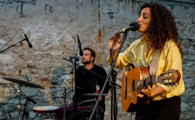 Genç bayan şarkıcı canlı performansta gitar çalıp şarkı söylüyor.