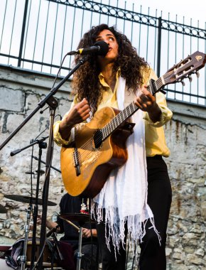 Genç bayan şarkıcı canlı performansta gitar çalıp şarkı söylüyor.