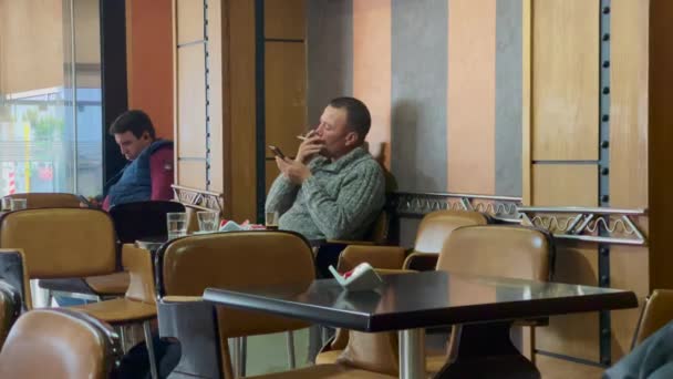 Καπνίζει Ένα Τσιγάρο Και Χρησιμοποιεί Κινητό Του Μια Καφετέρια — Αρχείο Βίντεο