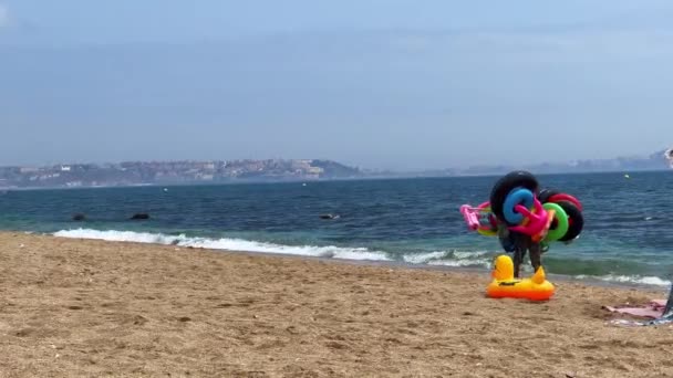 Man Walking Beach Selling Inflatable Water Toys — ストック動画