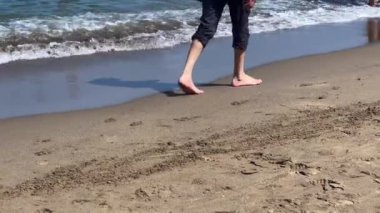 Man walking barefoot alongside the seashore