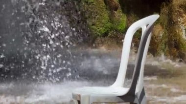 Su akıntısında plastik sandalye, arka planda şelale akıyor.