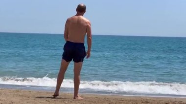 Denizin kenarında duran kaslı adam