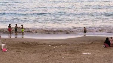 İnsanlar gün batımında sahilde eğleniyorlar.