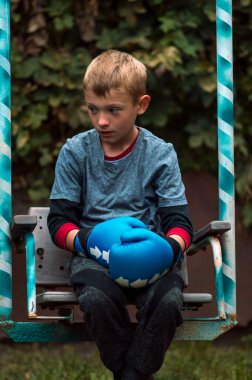 boy rests after training in blue gloves in the yard