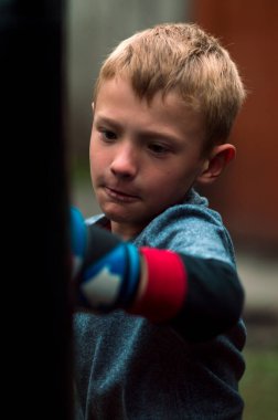 a boy punches a punching bag in blue gloves in the yard