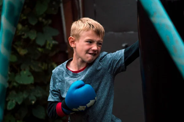 Boy Punches Punching Bag Blue Gloves Yard — Stockfoto