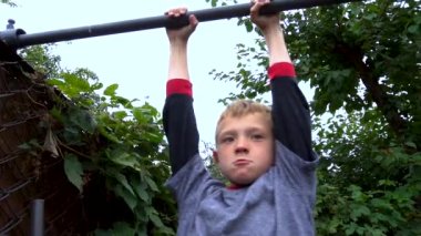 the boy does sports on the horizontal bar in the yard