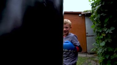 a boy punches a punching bag in blue gloves in the yard