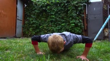 the boy does push-ups from the floor in the yard