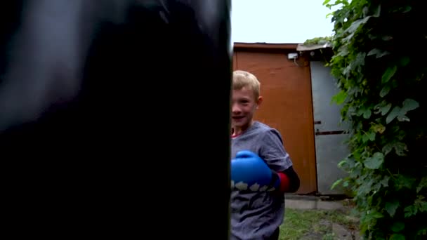 Boy Punches Punching Bag Blue Gloves Yard — Stockvideo