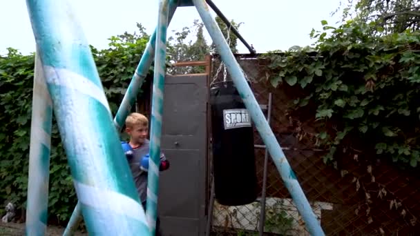 Boy Punches Punching Bag Blue Gloves Yard — Stockvideo