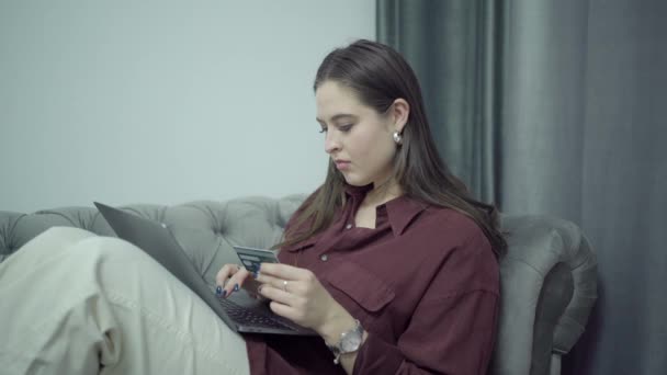 Hermosa mujer de compras en línea con una tarjeta de crédito con ordenador portátil en el regazo — Vídeos de Stock