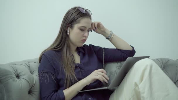 Серйозна бізнес-леді, що вводить ноутбук, сидить на дивані вдома — стокове відео