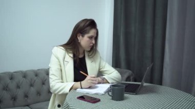 Dizüstü bilgisayarı olan bir kadın öğrenci evle ilgili notlar alıyor.