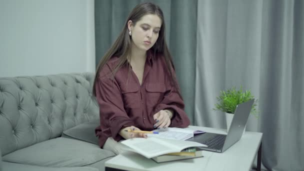 Frau auf Sofa mit Studentenbüchern und Laptop auf Couchtisch, häusliches Arbeitszimmer — Stockvideo