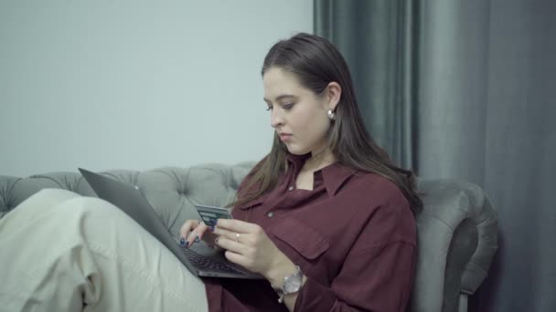 Hermosa mujer de compras en línea con una tarjeta de crédito con ordenador portátil en el regazo — Vídeo de stock