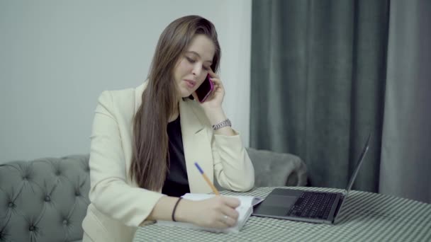 Chamada de mulher ao telefone, anotações em papéis em casa, laptop na mesa — Vídeo de Stock